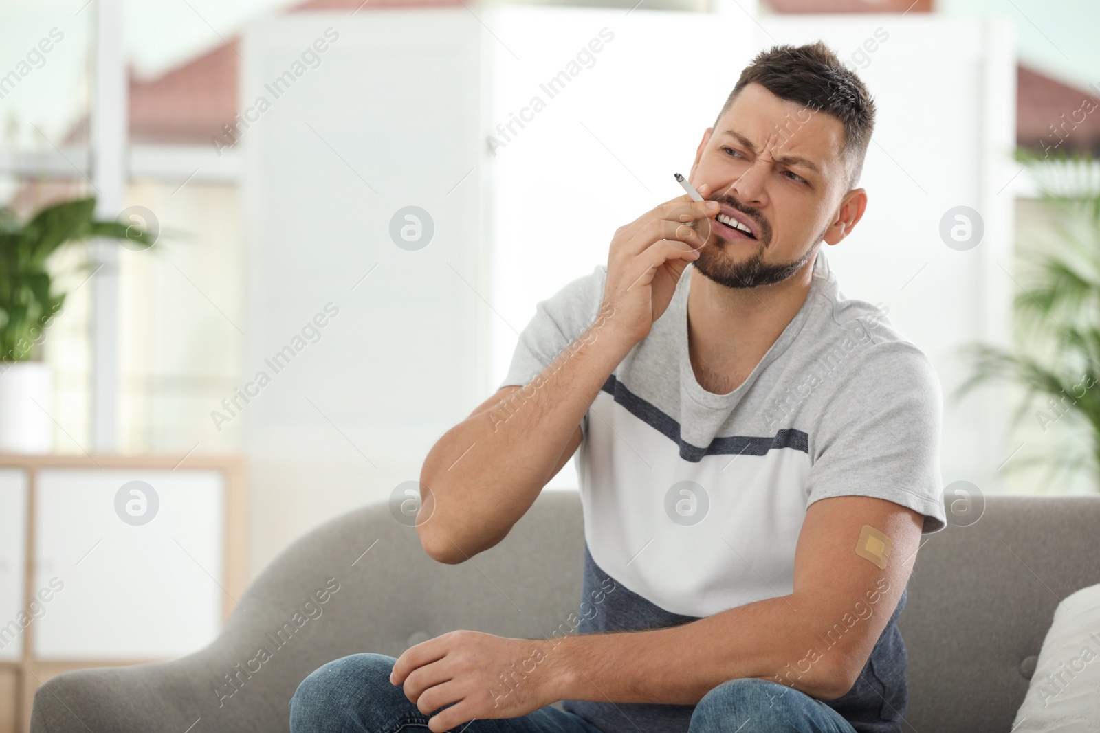 Photo of Emotional man with nicotine patch and cigarette at home