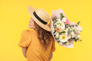 Photo of Happy woman in straw hat with bouquet of beautiful flowers on yellow background