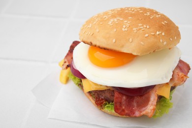 Photo of Delicious burger with fried egg on white tiled table, closeup. Space for text