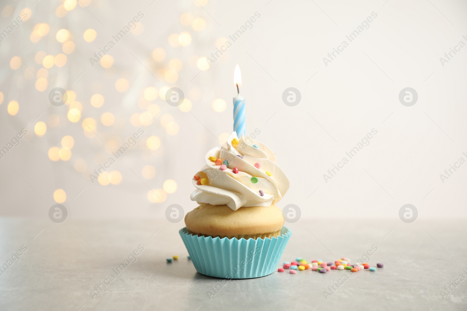 Photo of Birthday cupcake with candle on light grey table against blurred lights