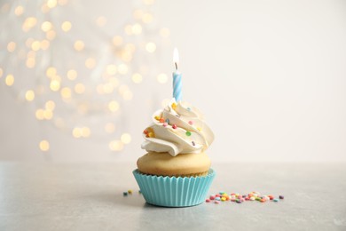 Photo of Birthday cupcake with candle on light grey table against blurred lights