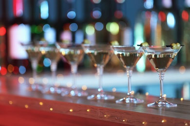 Photo of Glasses of martini cocktail with olives on counter in bar