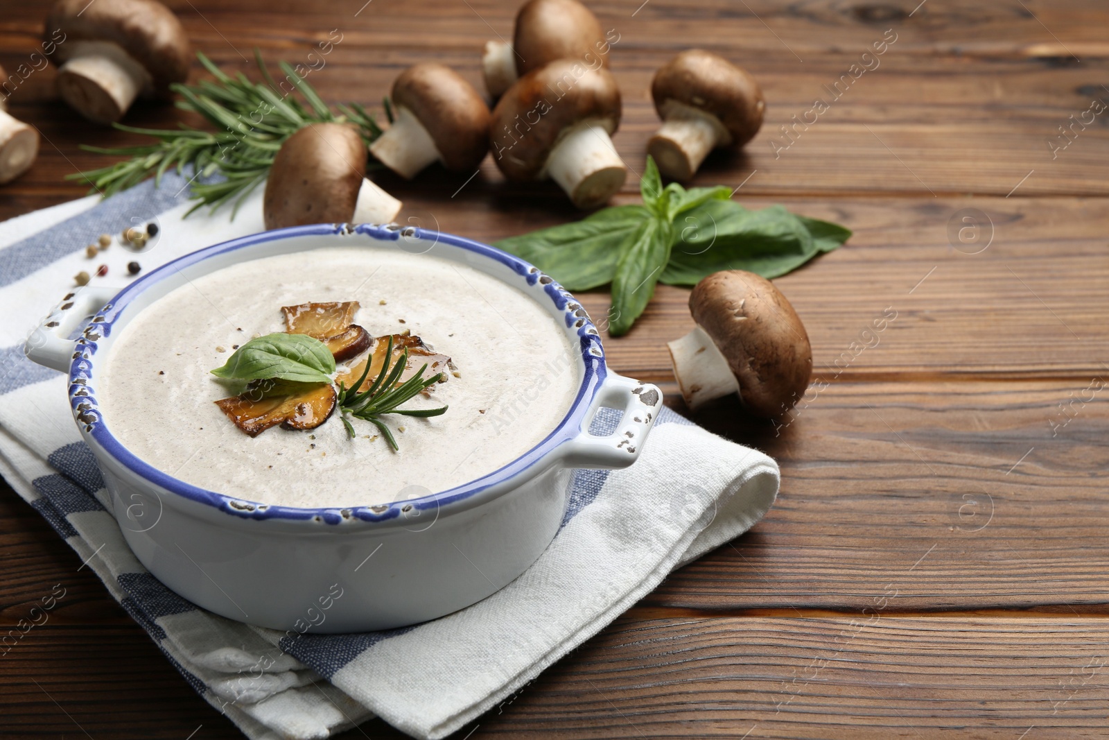 Photo of Delicious homemade mushroom soup in ceramic pot and fresh ingredients on wooden table. Space for text