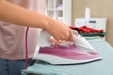 Photo of Young woman ironing clothes on board at home, closeup