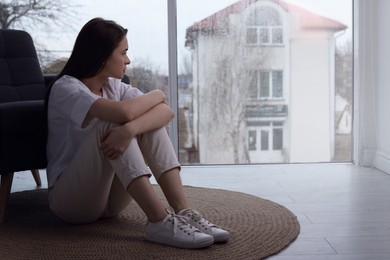 Melancholic young woman looking out of window indoors, space for text. Loneliness concept