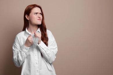 Photo of Angry woman popping bubble wrap on beige background, space for text. Stress relief