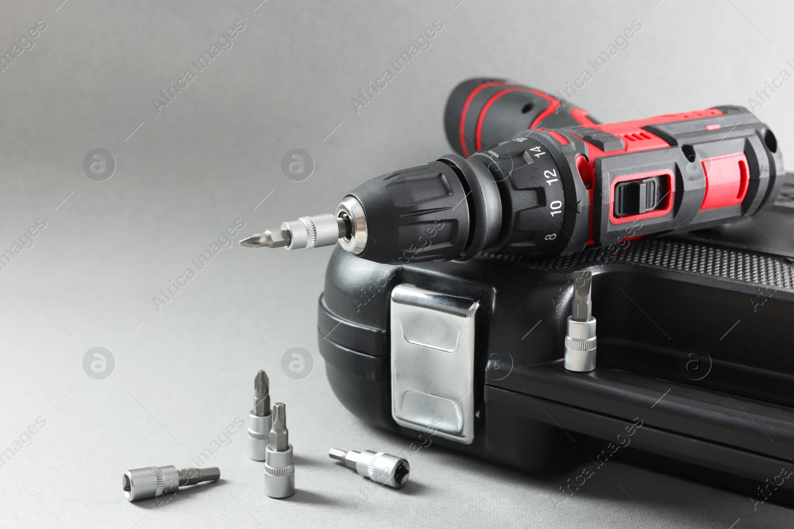 Photo of Electric screwdriver, drill bits and case on grey background. Space for text