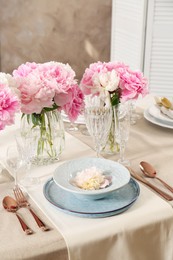 Stylish table setting with beautiful peonies and golden cutlery indoors