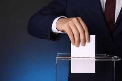 Man putting his vote into ballot box on dark blue background, closeup. Space for text