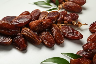 Tasty sweet dried dates and green leaves on white marble table, closeup