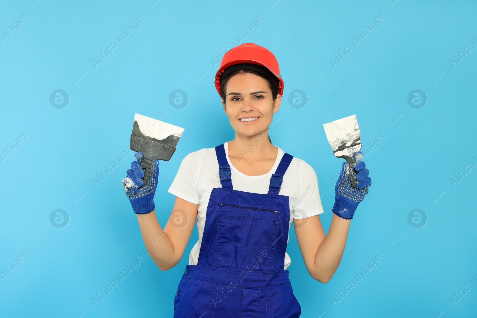 Photo of Professional worker in hard hat with putty knives on light blue background