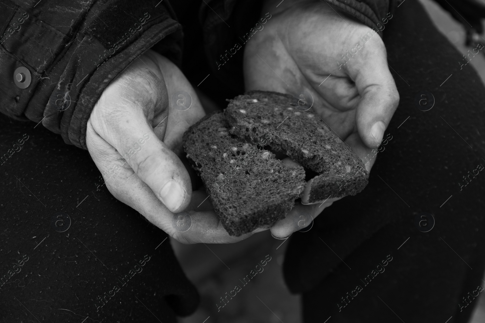 Photo of Poor homeless man holding piece of bread outdoors, closeup. Black and white effect