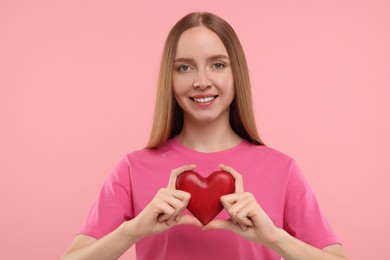 Happy young woman holding red heart on pink background