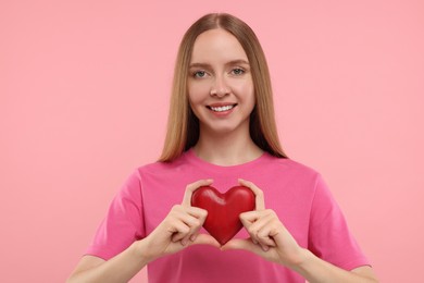 Photo of Happy young woman holding red heart on pink background