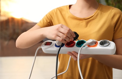 Woman inserting power plug into extension cord indoors, closeup. Electrician's professional equipment