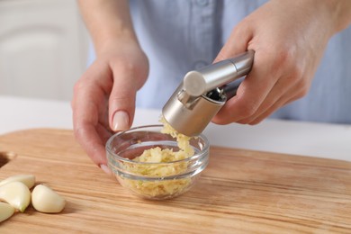 Photo of Woman squeezing garlic with press at wooden table indoors, closeup