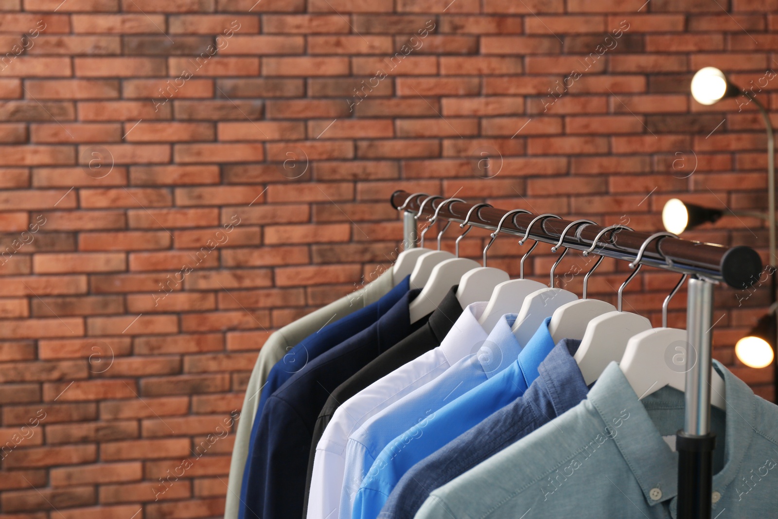 Photo of Wardrobe rack with stylish clothes near brick wall. Space for text