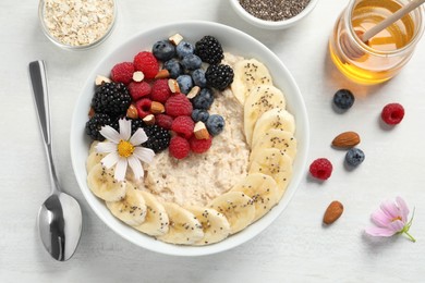 Photo of Tasty oatmeal porridge with berries, banana and chia seeds served on light wooden table, flat lay