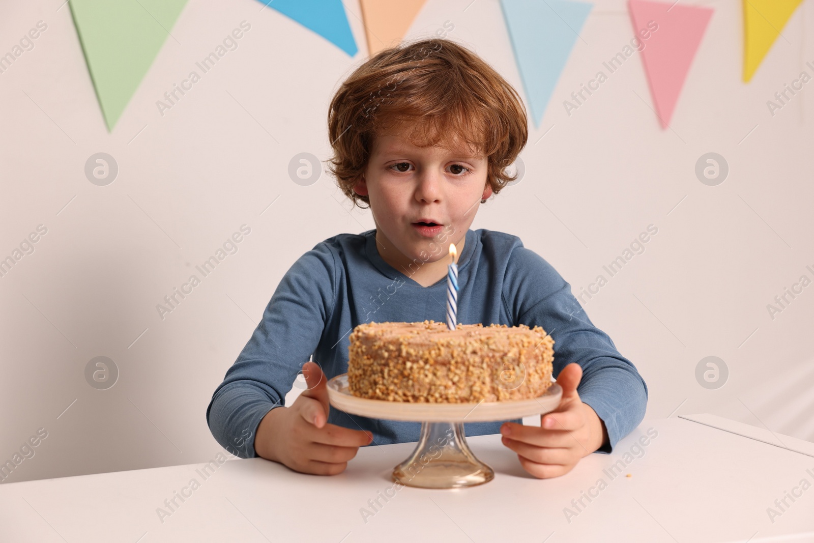 Photo of Cute boy with birthday cake at white table indoors