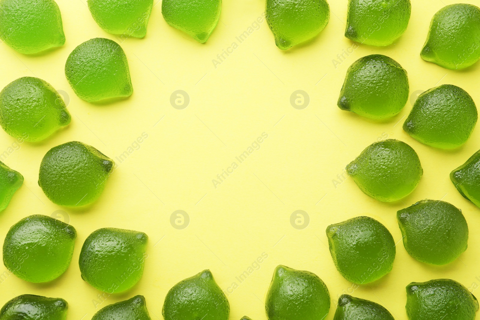 Photo of Frame of delicious gummy lime candies on green background, flat lay. Space for text
