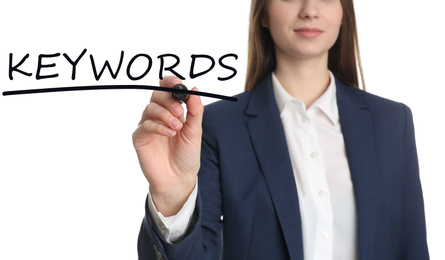 Woman writing word KEYWORDS on transparent board against white background, closeup