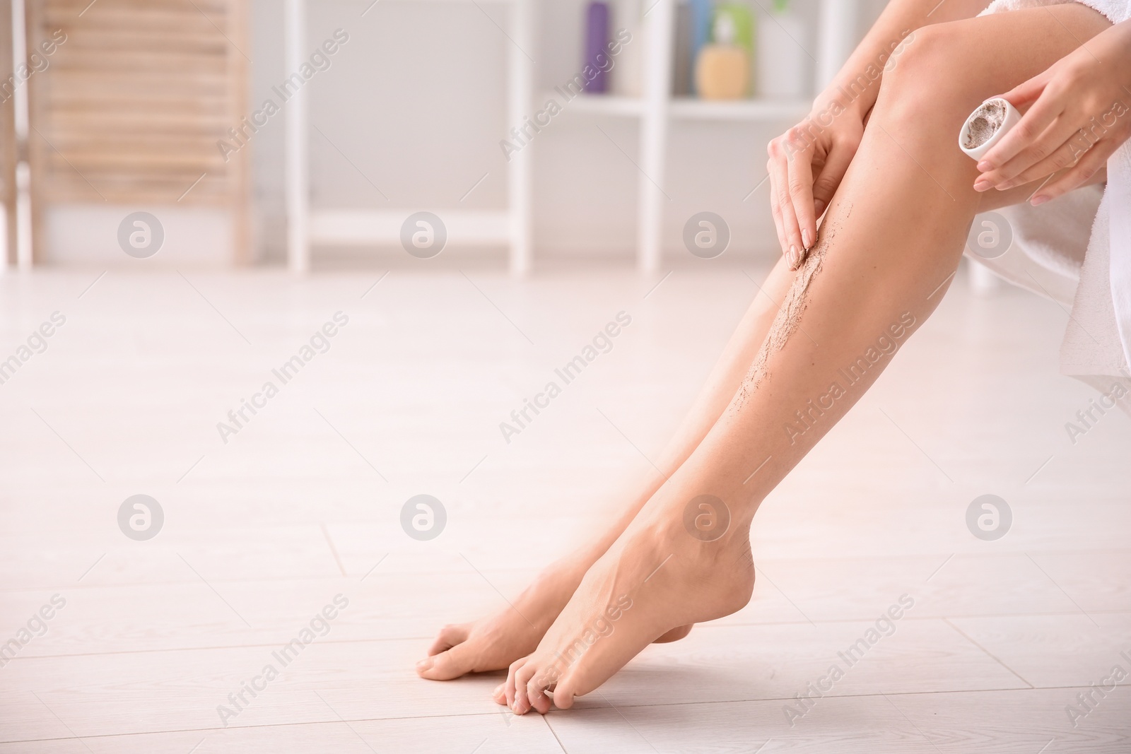 Photo of Woman applying body scrub on legs at home