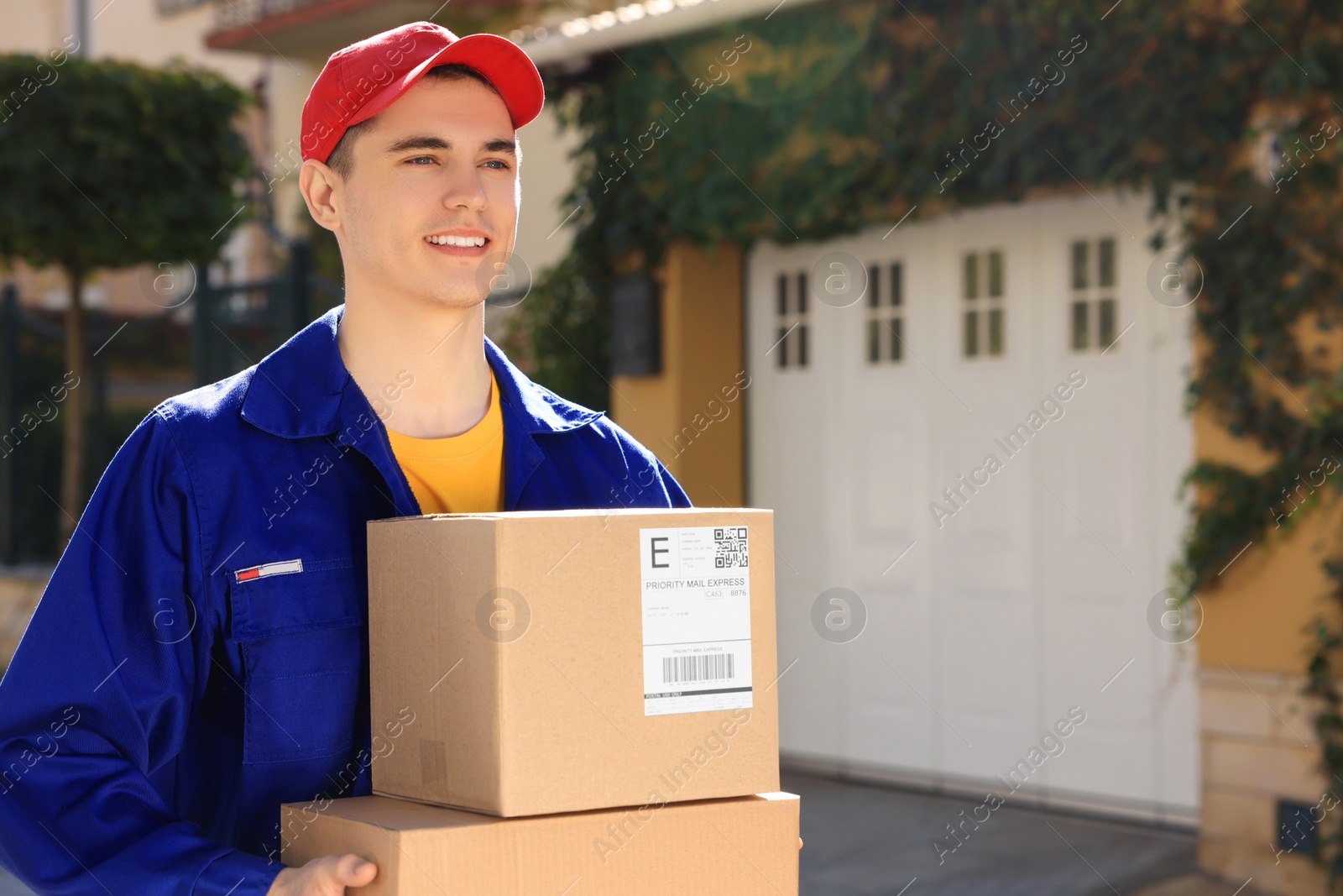 Photo of Courier carrying cardboard boxes near house on city street