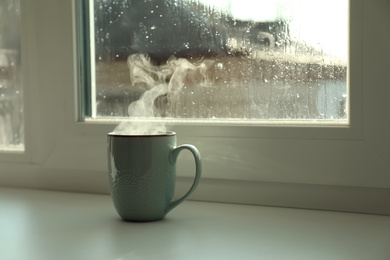 Photo of Cup of hot drink near window on rainy day. Space for text