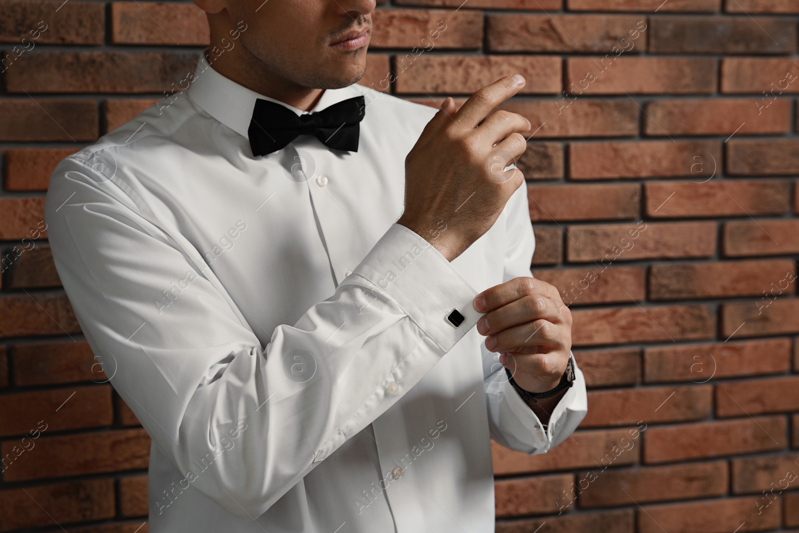 Photo of Stylish man putting on cufflink near brick wall, closeup