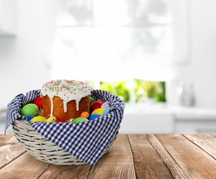 Image of Traditional Easter cake and dyed eggs in basket on wooden table indoors. Space for text