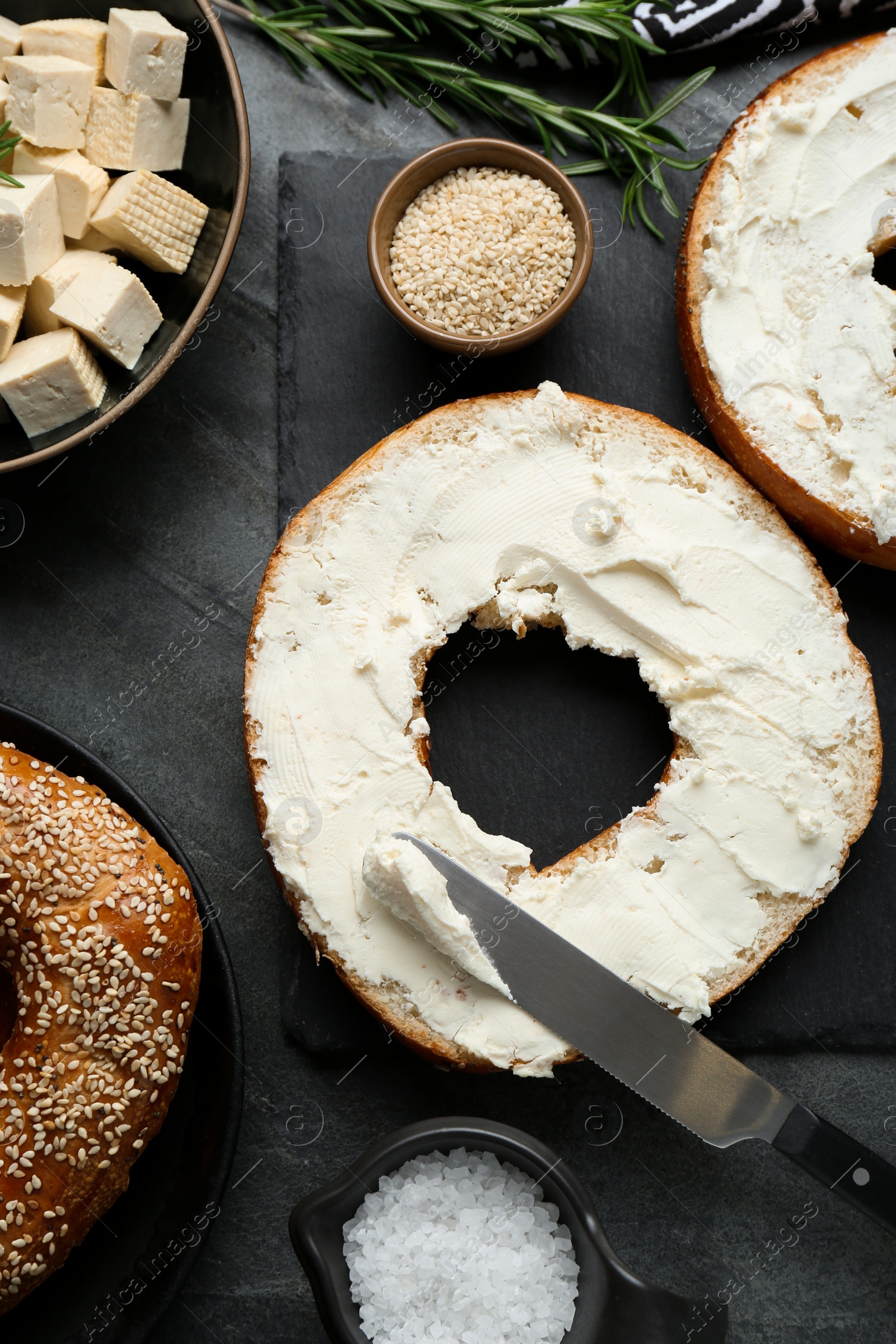 Photo of Delicious bagels with tofu cream cheese, sesame seeds and salt on black table, flat lay