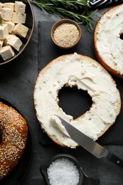 Photo of Delicious bagels with tofu cream cheese, sesame seeds and salt on black table, flat lay