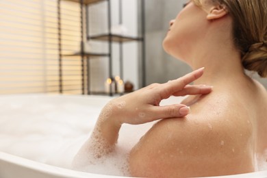 Photo of Woman taking bath with foam in tub indoors, closeup. Space for text