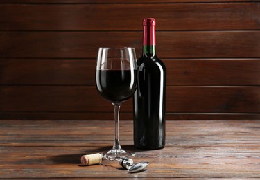 Photo of Corkscrew, glass and bottle of red wine on wooden table