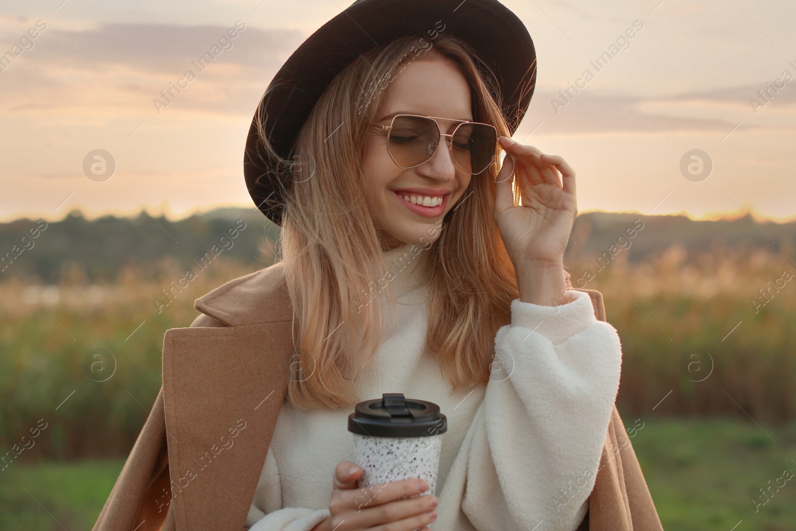 Photo of Beautiful young woman with cup of coffee wearing stylish autumn clothes outdoors