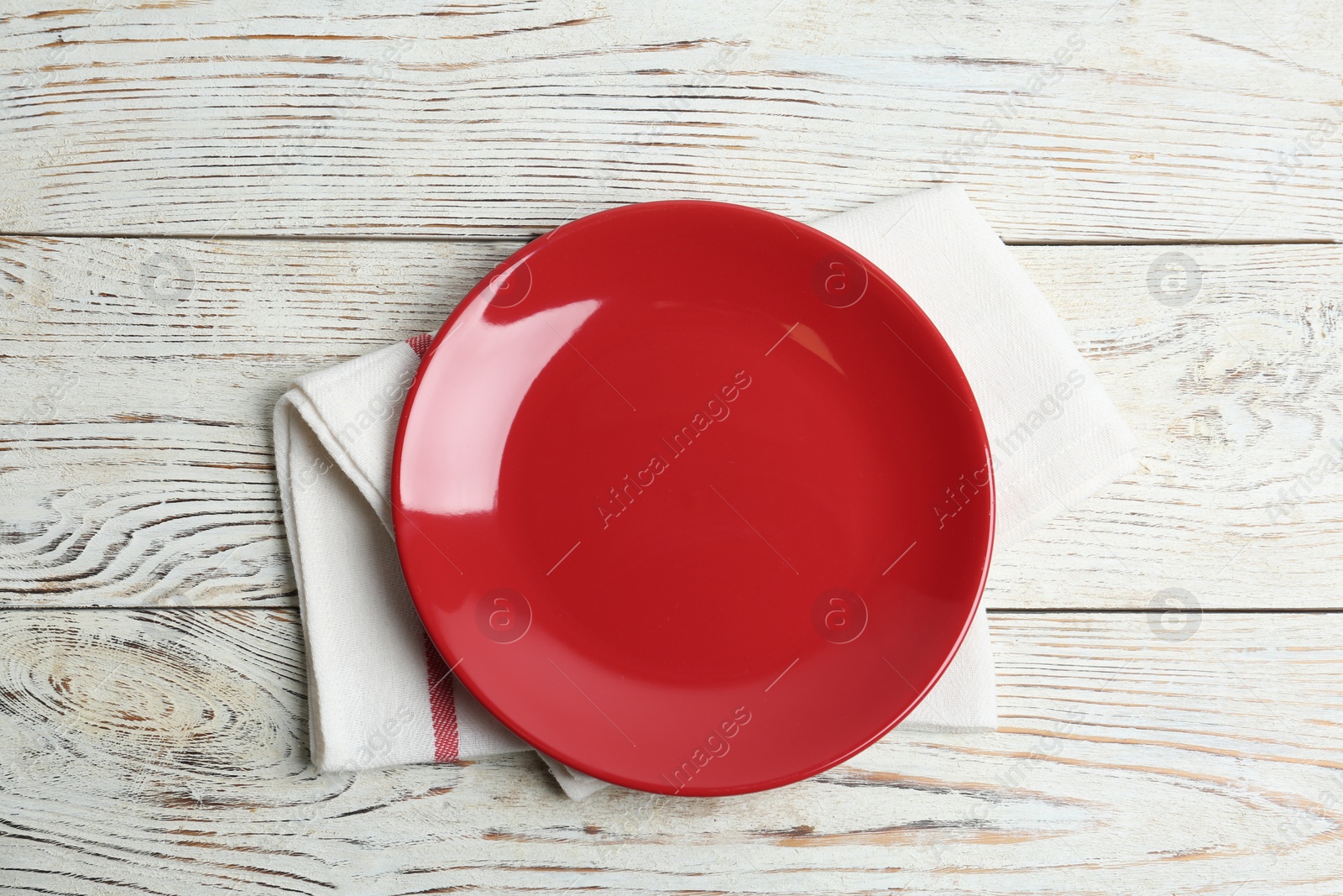 Photo of Empty red plate and napkin on white wooden table, flat lay