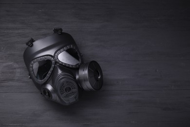 One gas mask on black wooden background, top view. Space for text