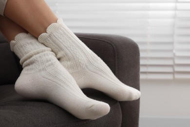 Photo of Woman in warm socks relaxing on armchair at home, closeup. Space for text