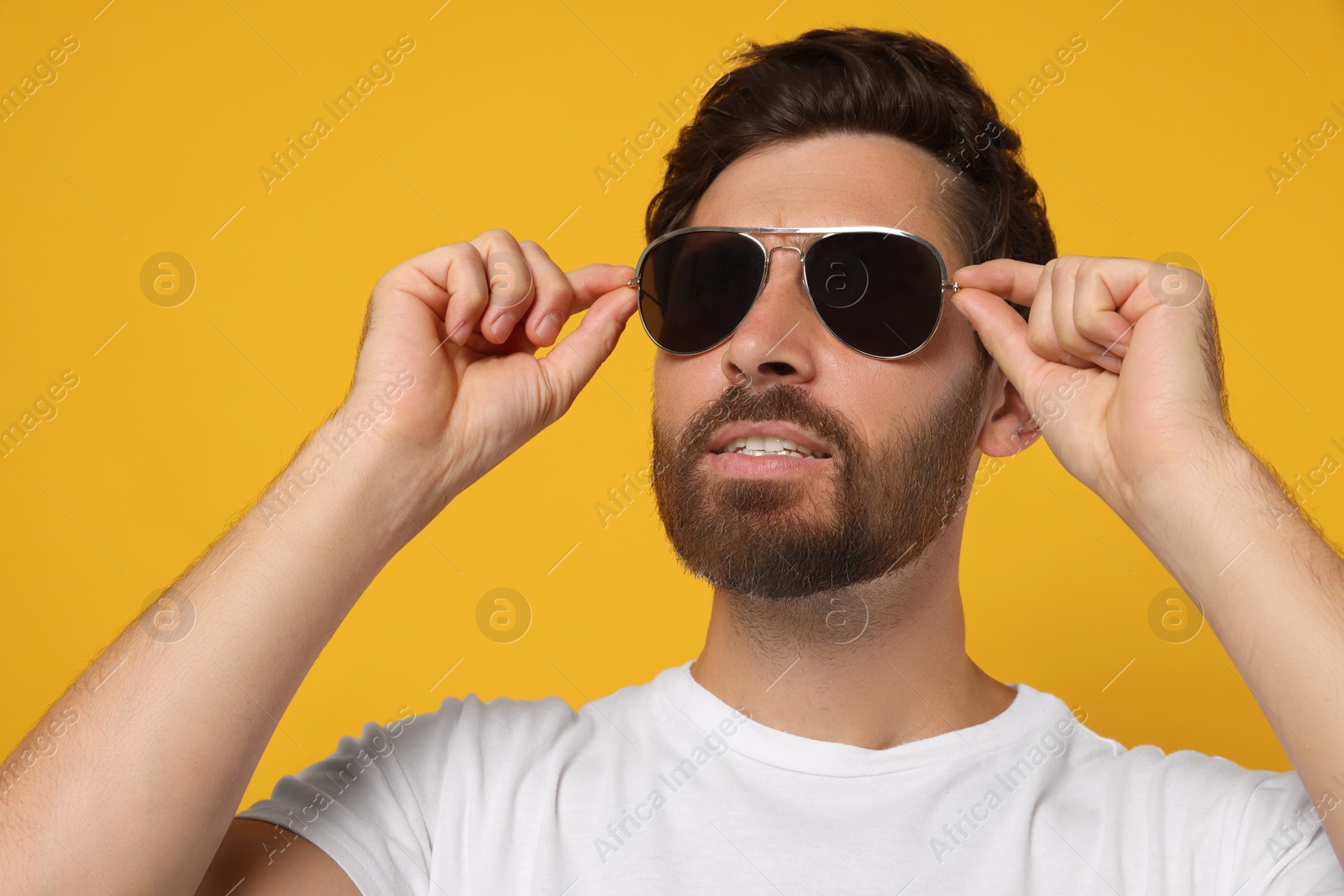 Photo of Portrait of bearded man with stylish sunglasses on orange background, closeup