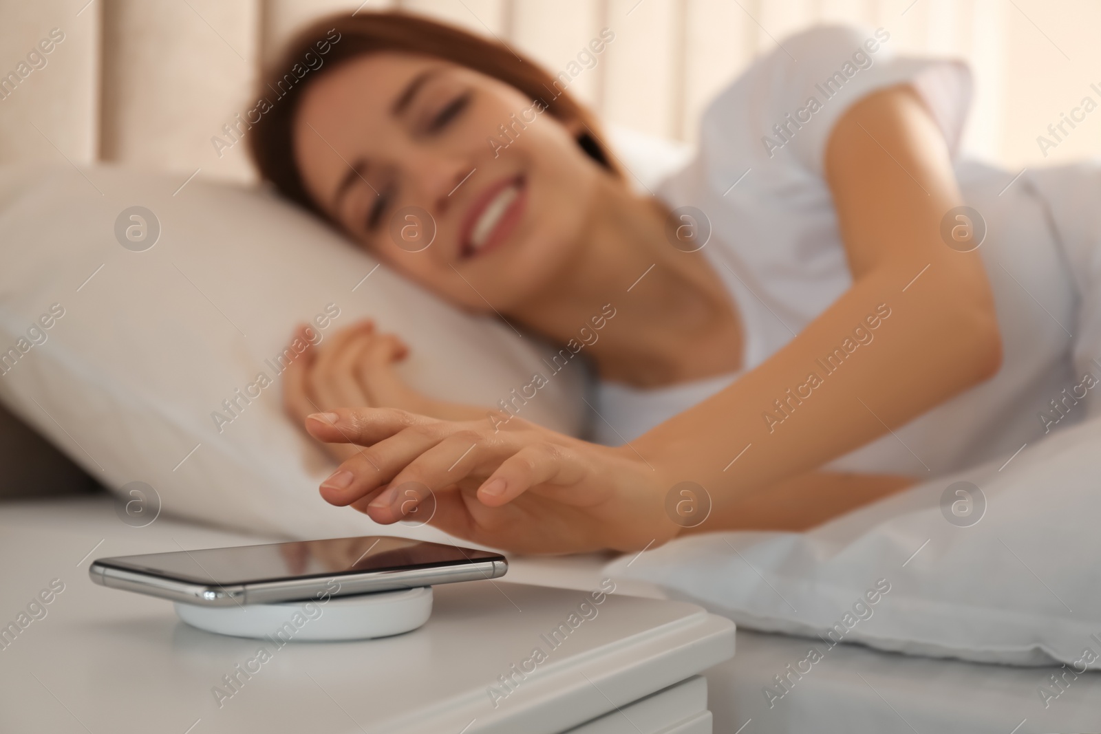 Photo of Woman taking smartphone from wireless charger in bedroom