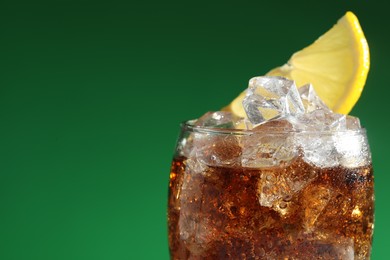 Photo of Glass of refreshing soda drink with ice cubes and lemon on green background, closeup. Space for text