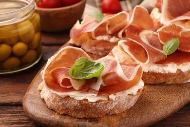 Photo of Board of tasty sandwiches with cured ham, basil and cream cheese on wooden table, closeup