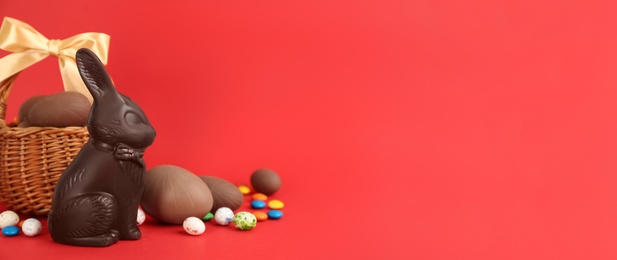Photo of Chocolate Easter bunny, eggs and candies on red background. Space for text