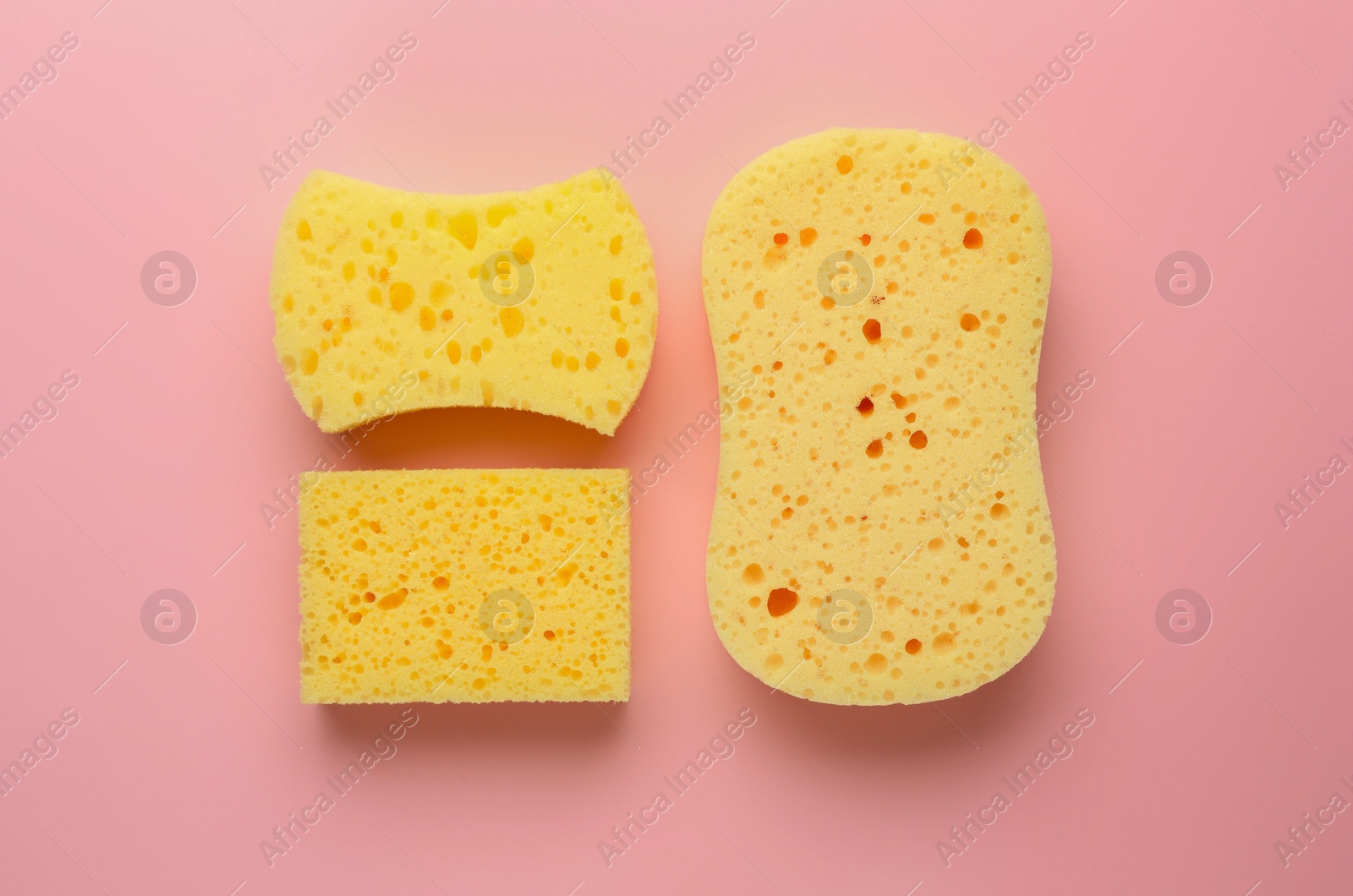 Photo of New yellow sponges of different shapes on pink background, flat lay