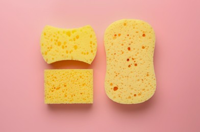 New yellow sponges of different shapes on pink background, flat lay