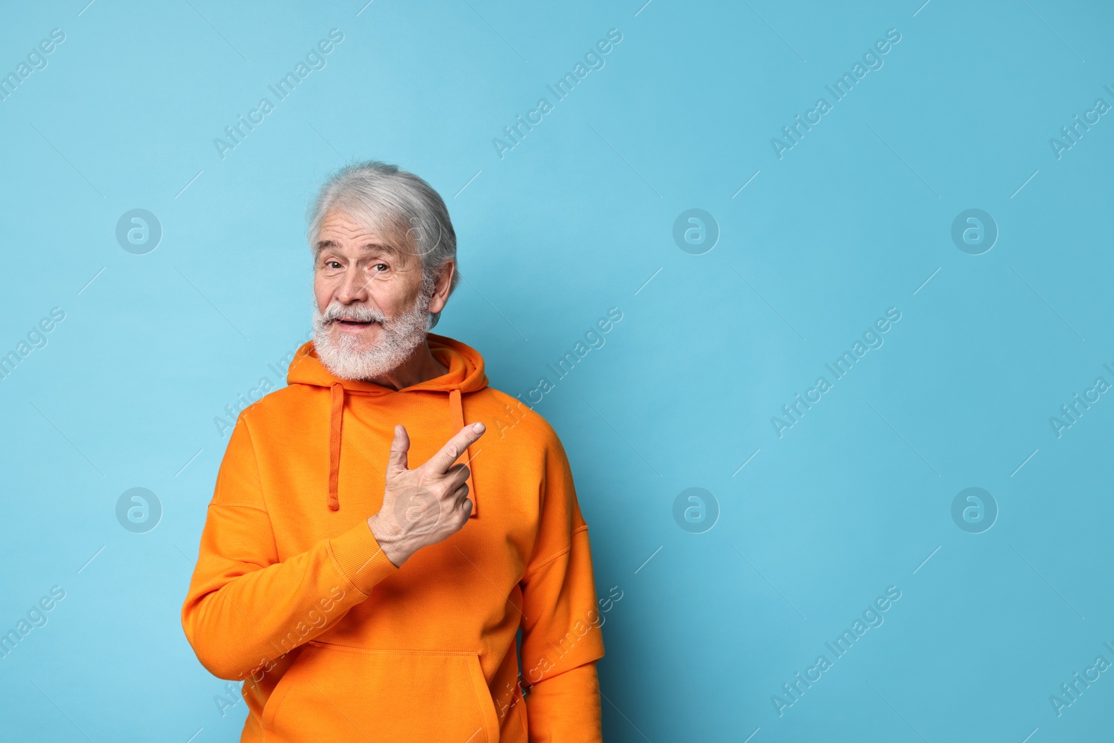 Photo of Senior man with mustache pointing at something on light blue background, space for text