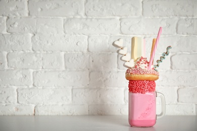Photo of Tasty milk shake with sweets in mason jar on table near brick wall. Space for text