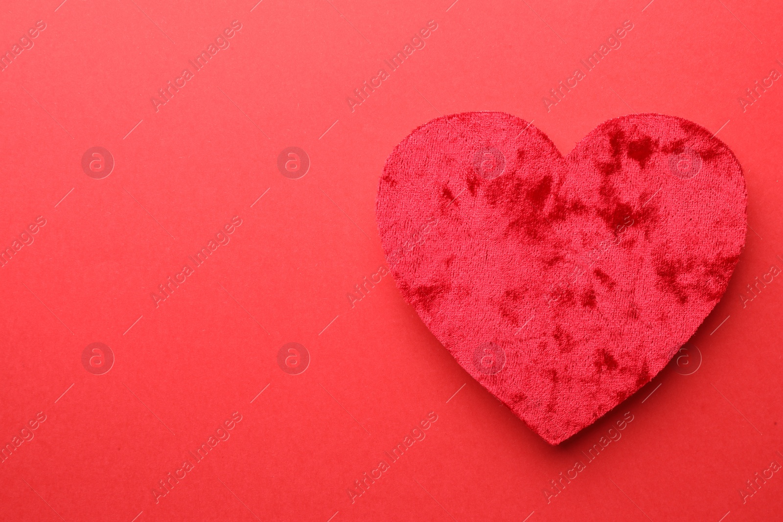 Photo of One velvet heart on red background, top view. Space for text