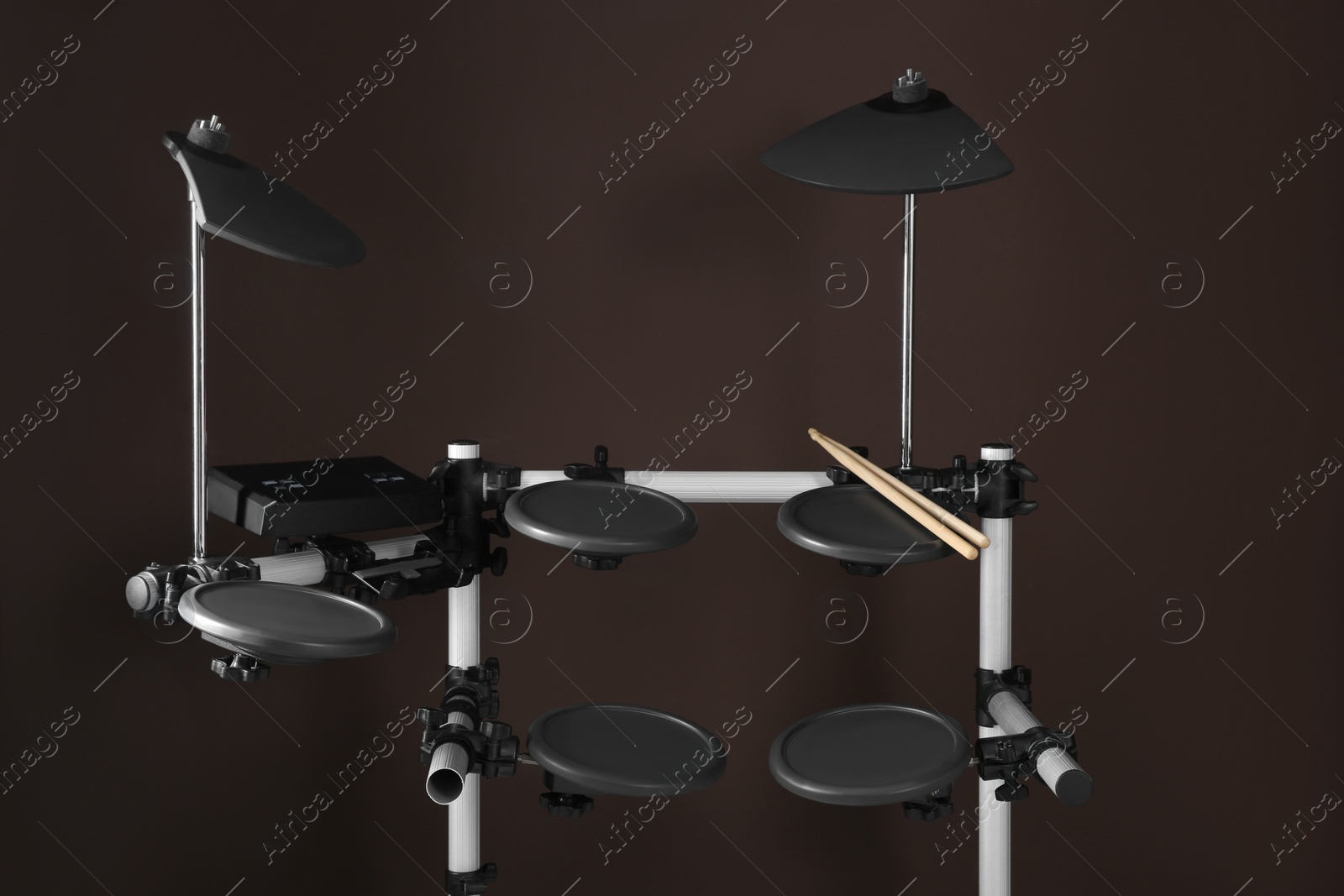 Photo of Modern electronic drum kit with sticks on brown background. Music instrument
