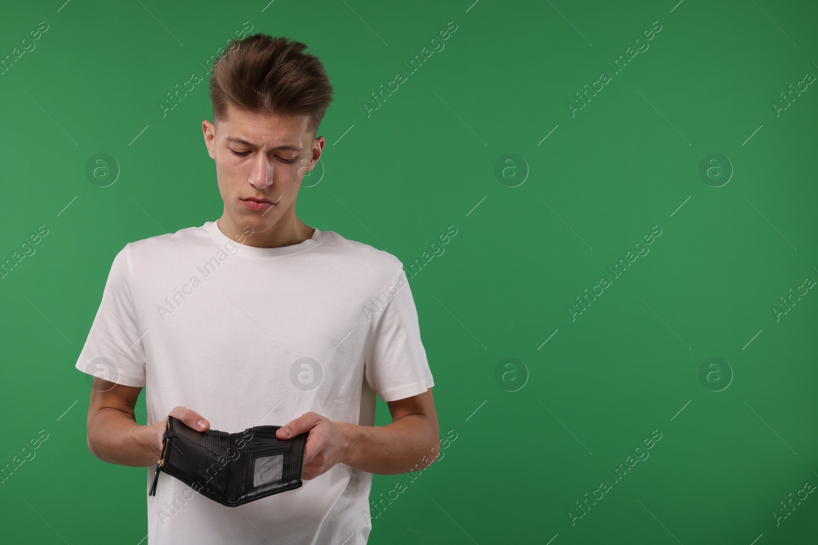 Photo of Upset man with empty wallet on green background. Space for text